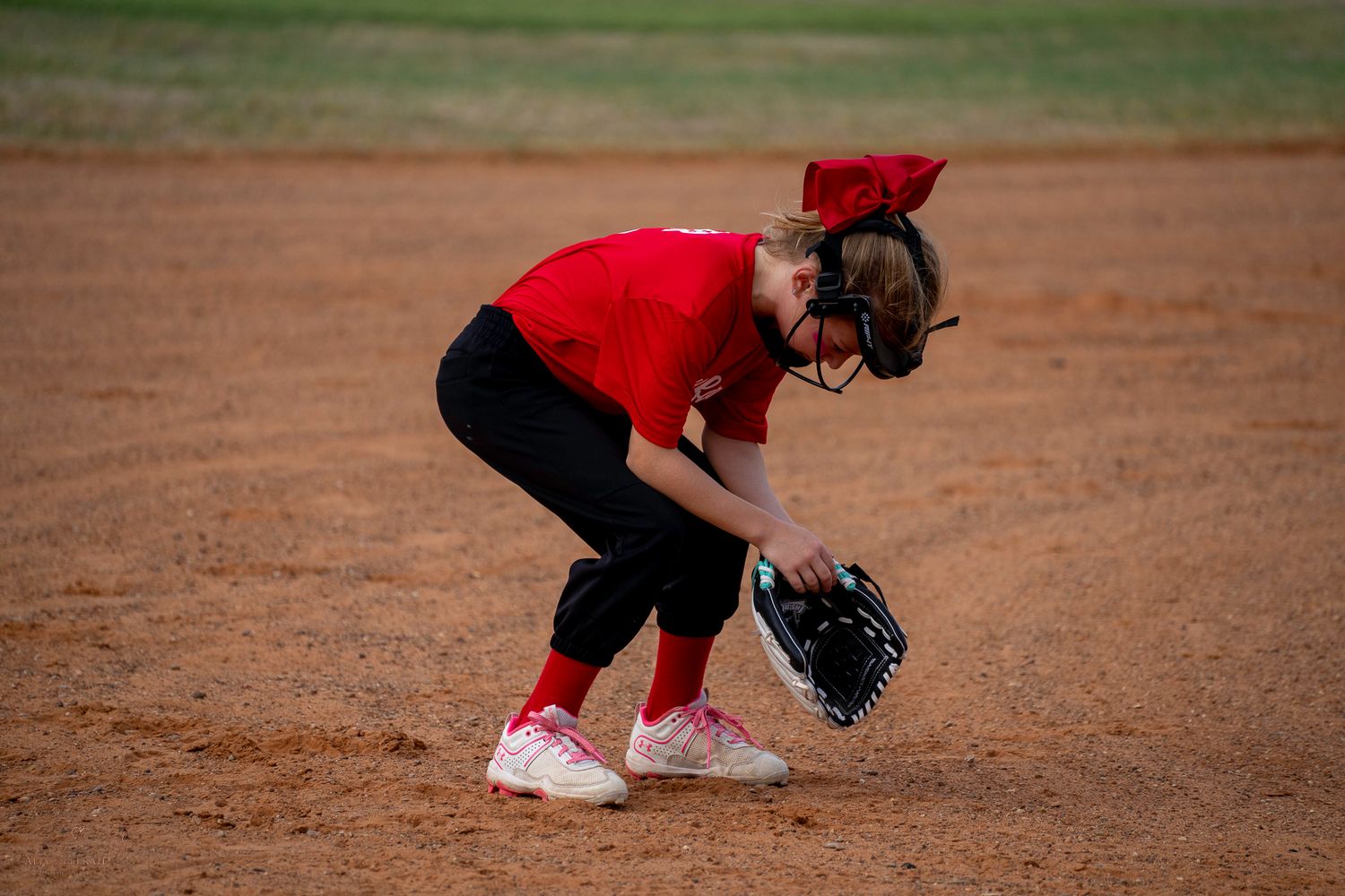 A player in red and black uniform fields a ground ball on a softball diamond.