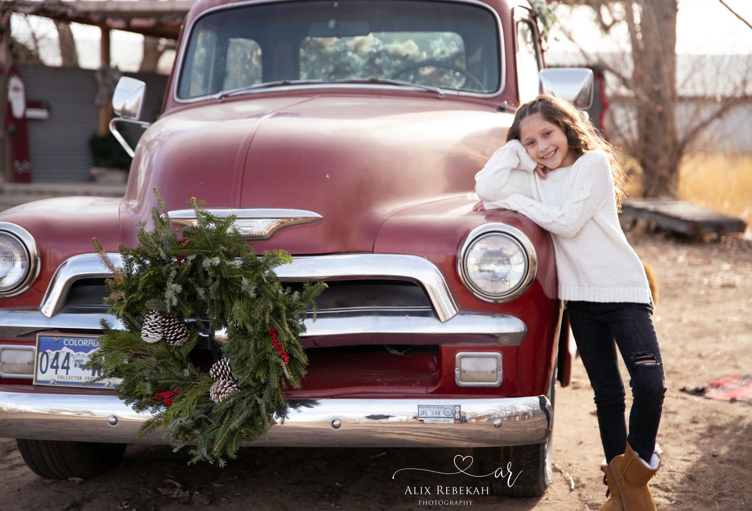 Vintage red GMC pickup truck decorated with Christmas wreath in rustic setting.