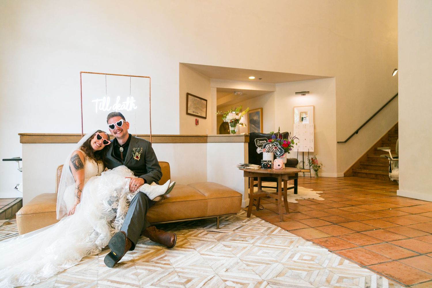 Couple sits together on white couch in elegant room during wedding celebration.