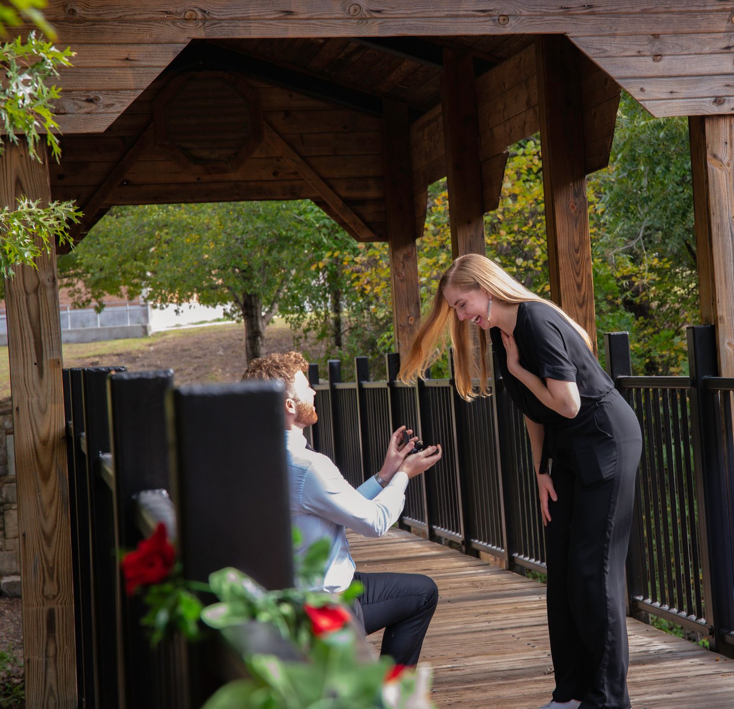Two people share a playful moment on a wooden covered deck surrounded by greenery and flowers.