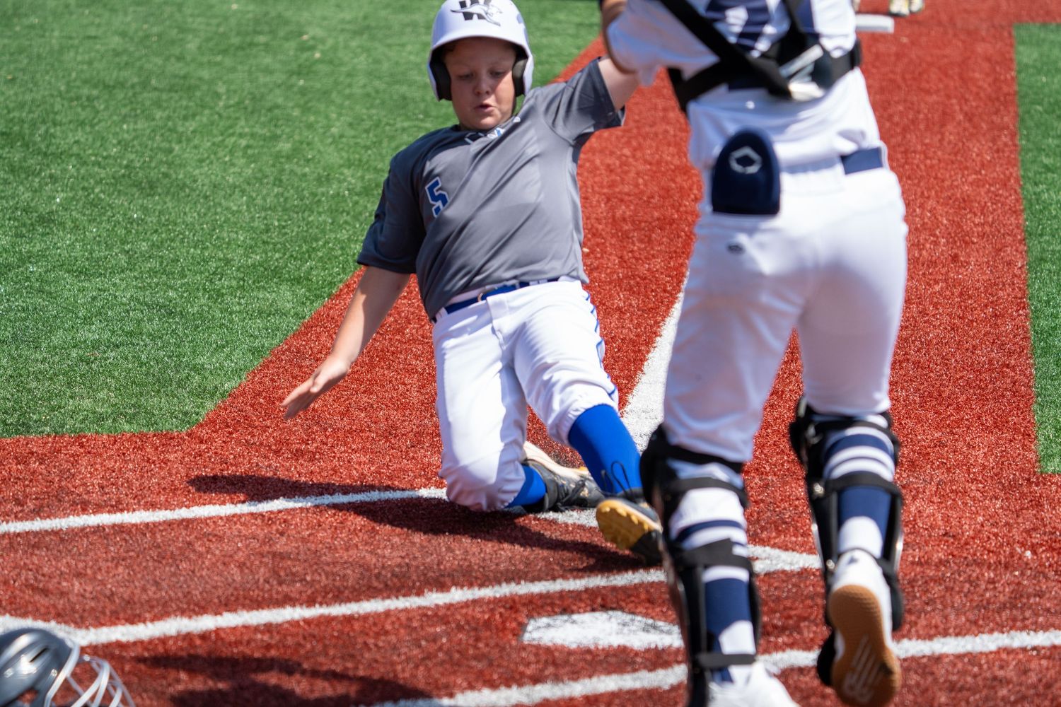 Baseball player sliding into home plate during competitive game on artificial turf field.