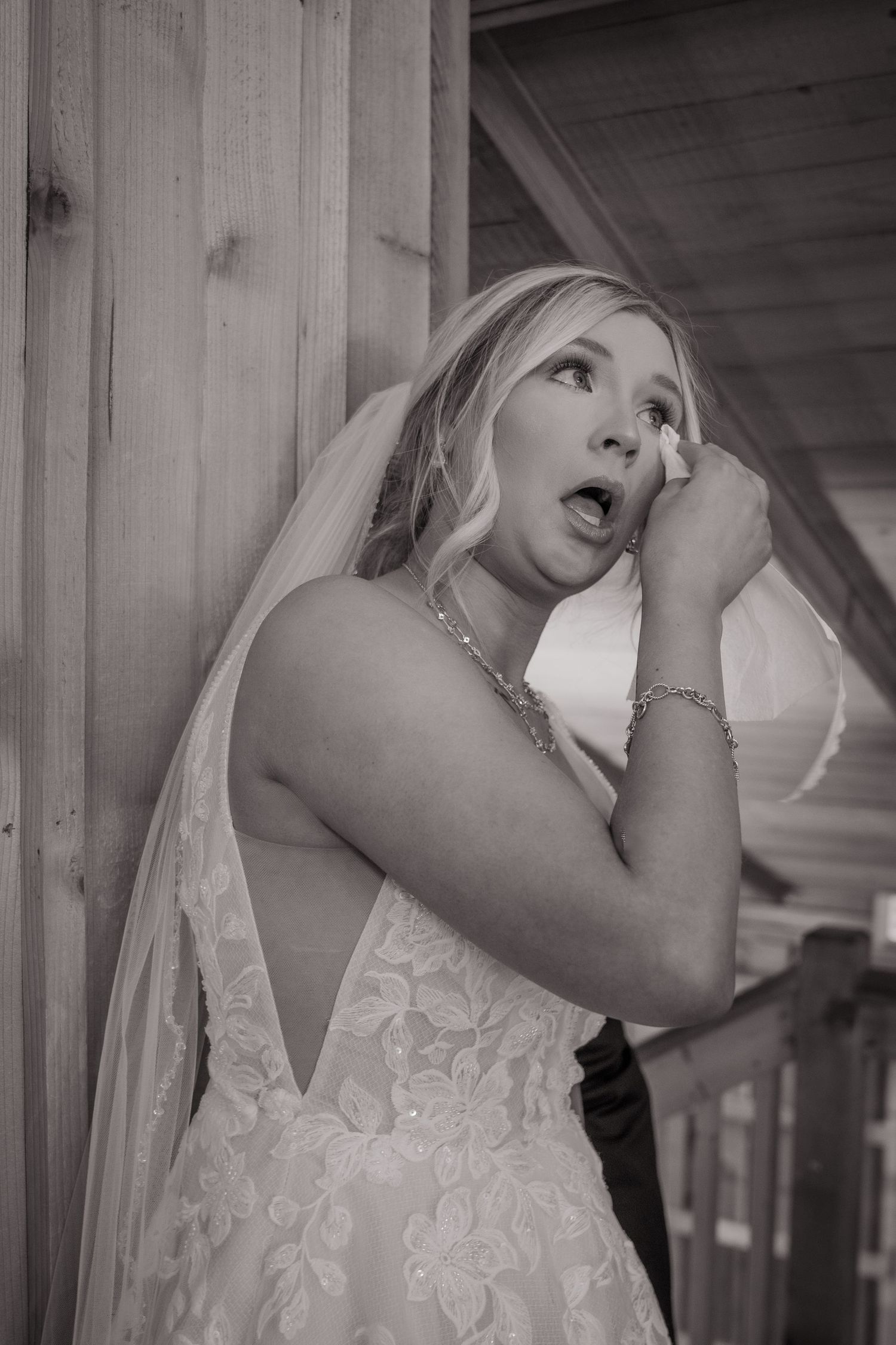 A bride in a lace wedding dress with a veil shows an emotional expression in a black and white photograph.