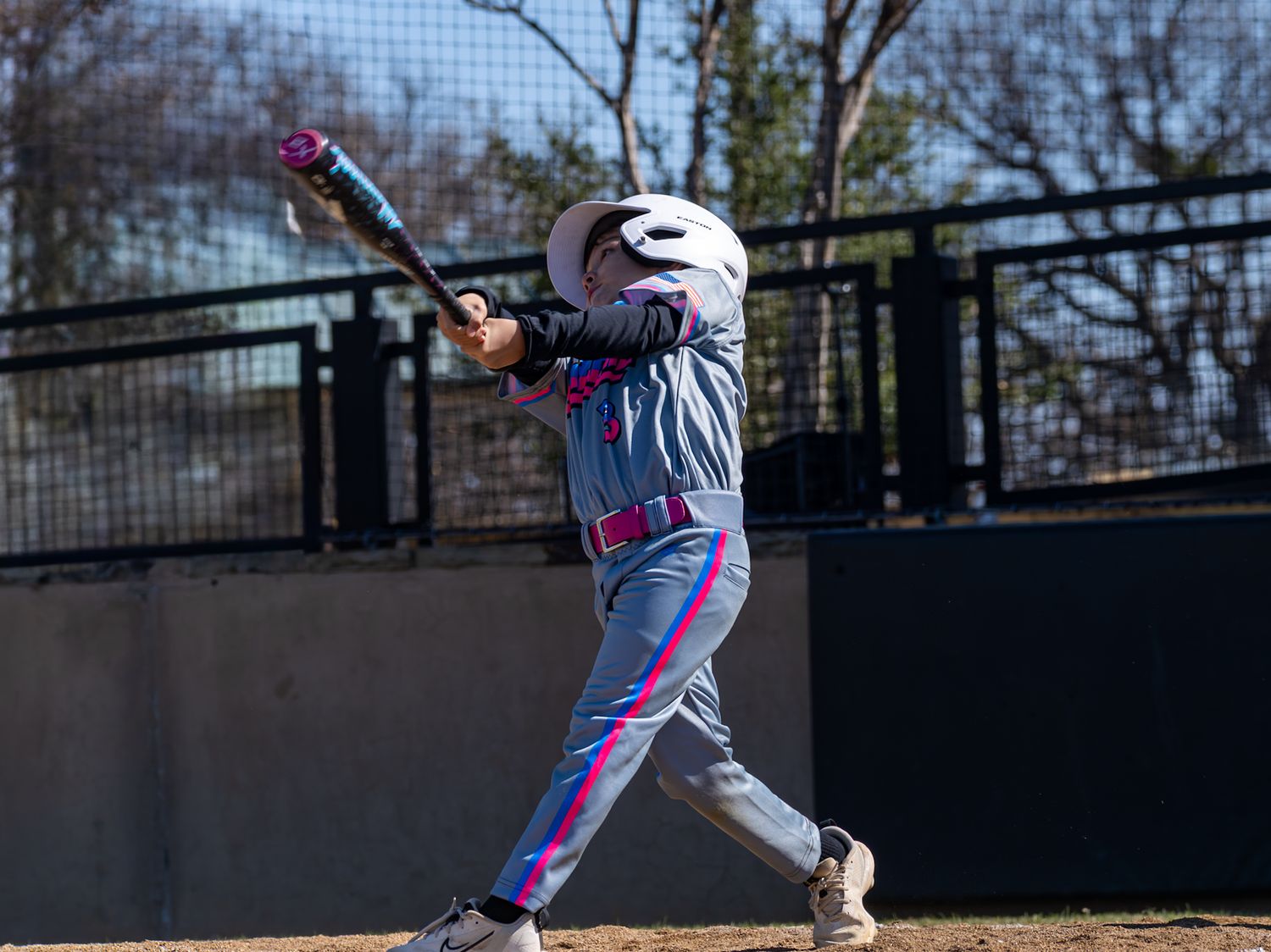 Baseball player in gray and pink uniform swinging bat during a game outdoors.