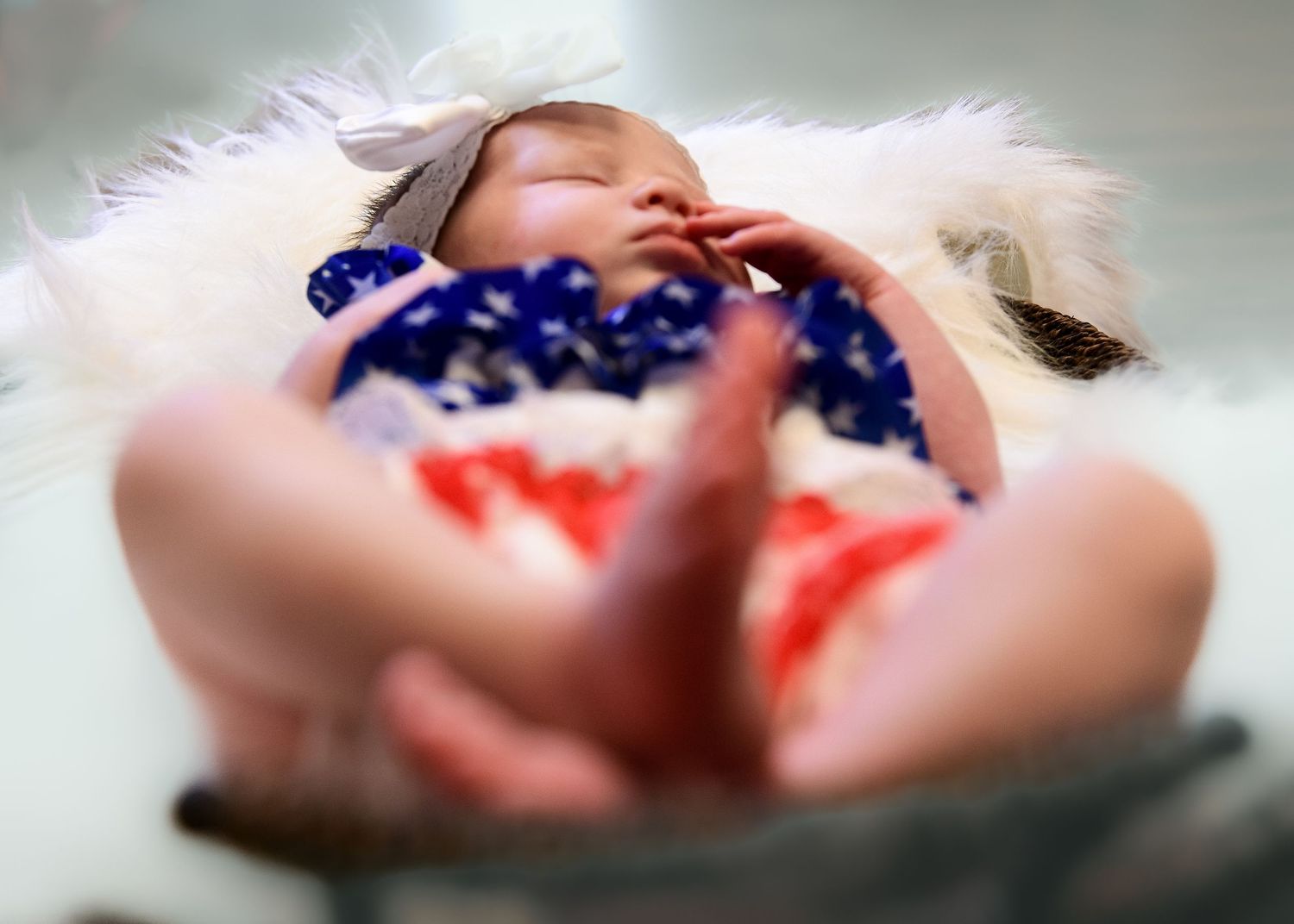 Newborn sleeping peacefully on white fur with patriotic red white and blue styling.