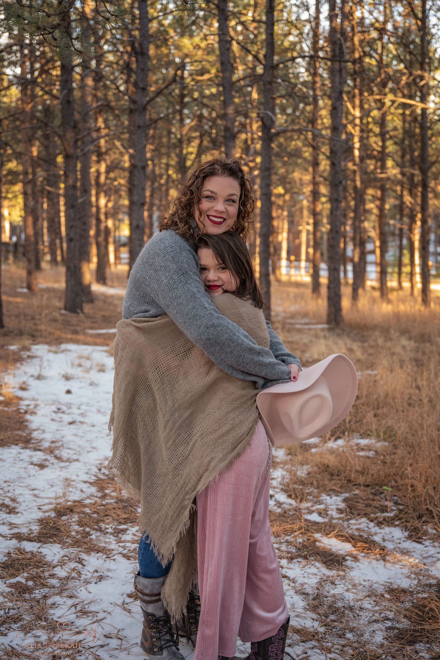 Joyful moment between two people hugging in winter forest with golden sunlight through trees.