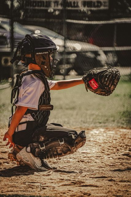 Young baseball catcher in protective gear crouching on baseball diamond.
