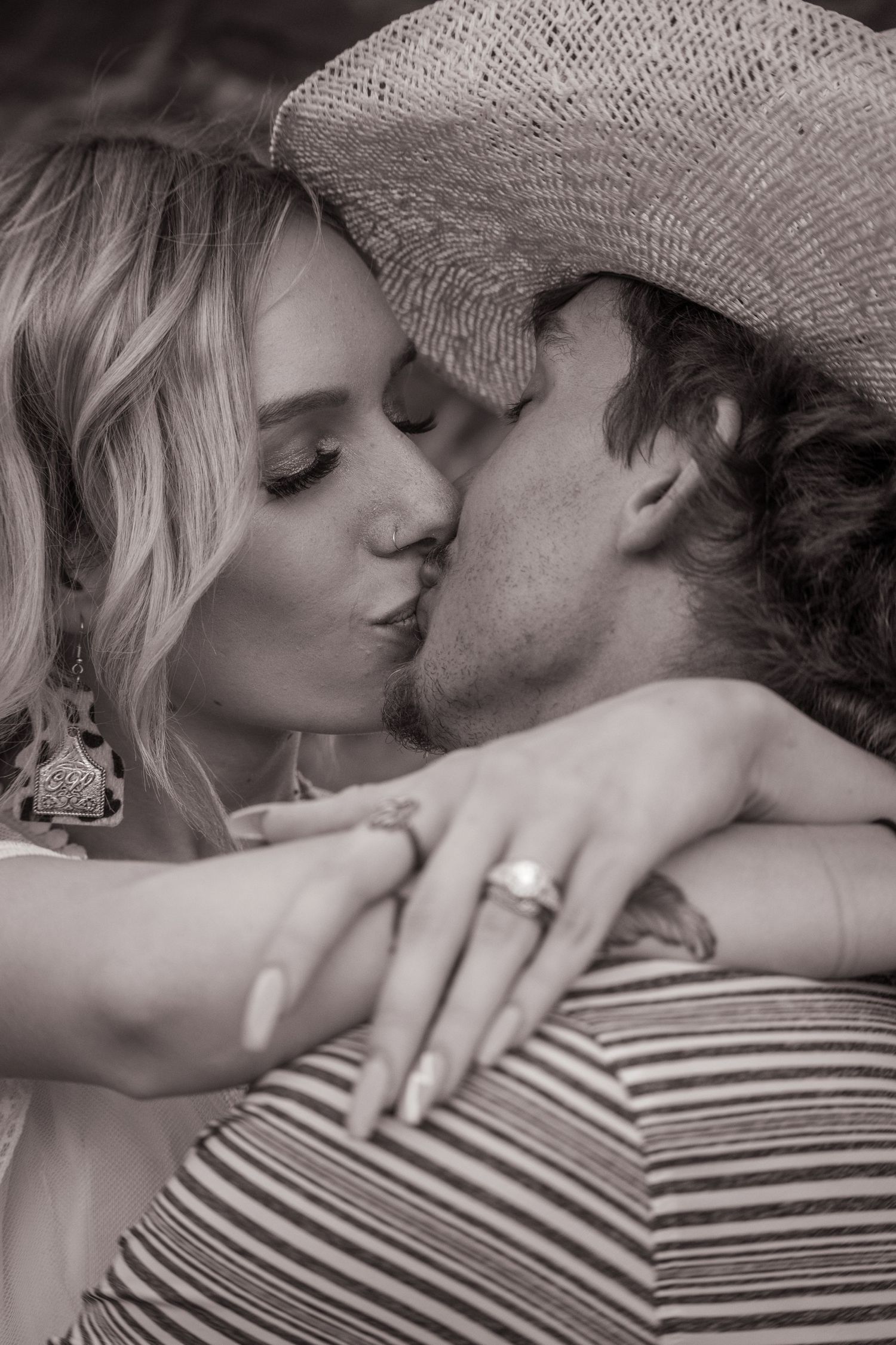 Black and white romantic portrait showing couple kissing while wearing cowboy hat.