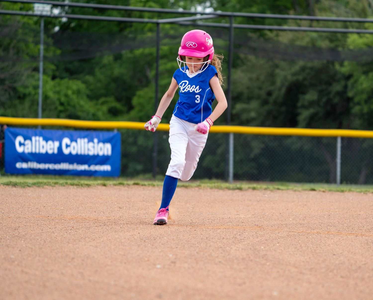 Youth baseball player in blue and white uniform fields a ground ball during a game on dirt infield.