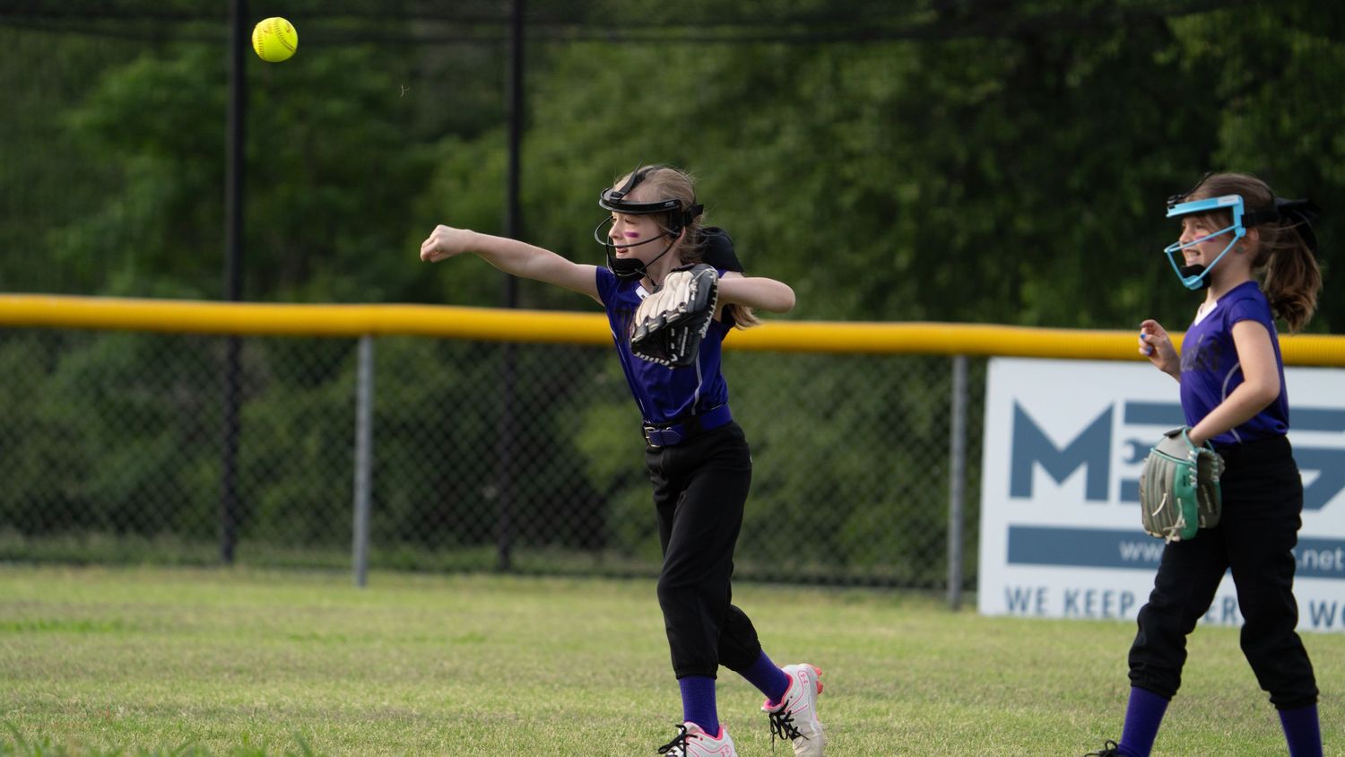 A sequence of softball players practicing batting form and swinging at a yellow ball on a sunny field.