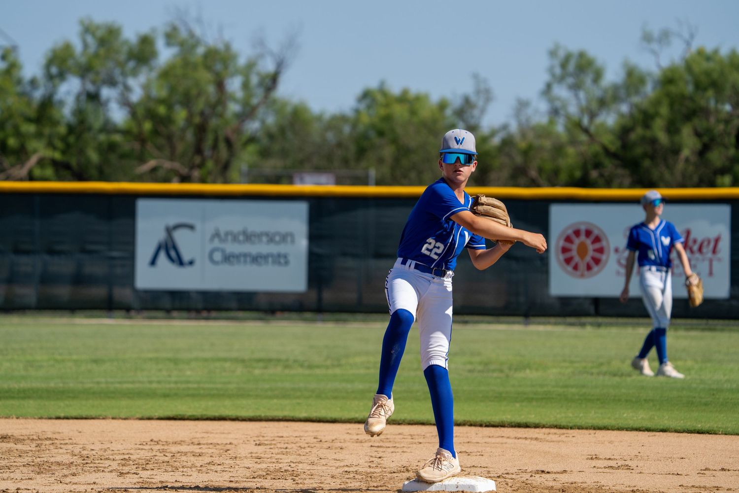 A baseball player in blue throws a pitch from the mound during a game on a sunny day.