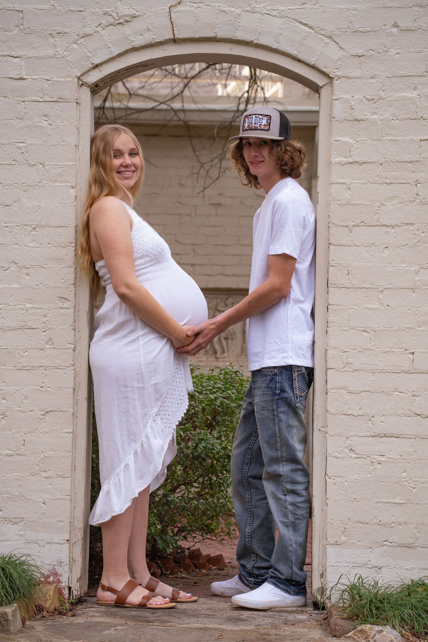 A series of outdoor photos showing a happy couple in white clothing having a romantic moment against a white brick wall.