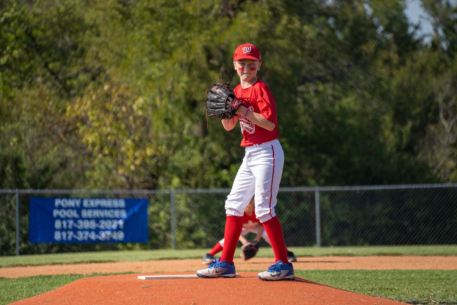 Baseball player in red uniform standing on pitchers mound preparing to throw during game at outdoor baseball field.