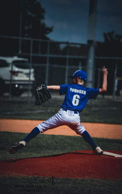 Baseball player in blue uniform stretches dramatically on pitcher's mound with glove extended during game practice.