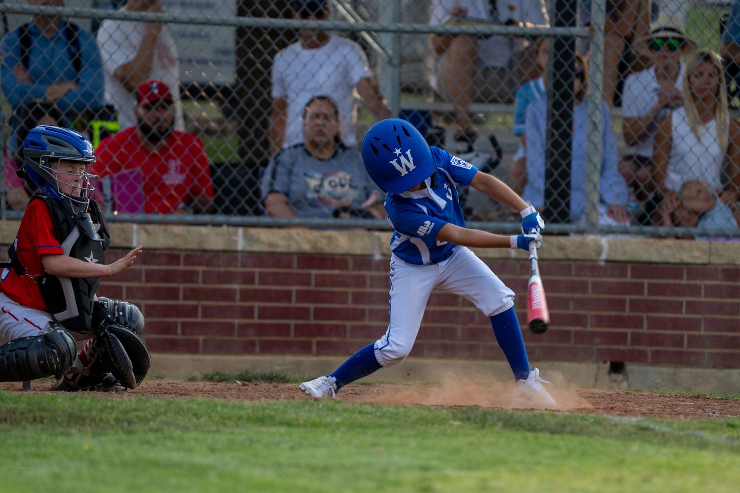 Baseball batter in blue uniform swings bat during game while catcher in red crouches behind home plate.