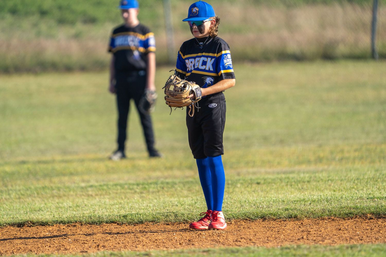 A little league baseball player stands at the pitchers mound during a youth baseball game on a sunny day.