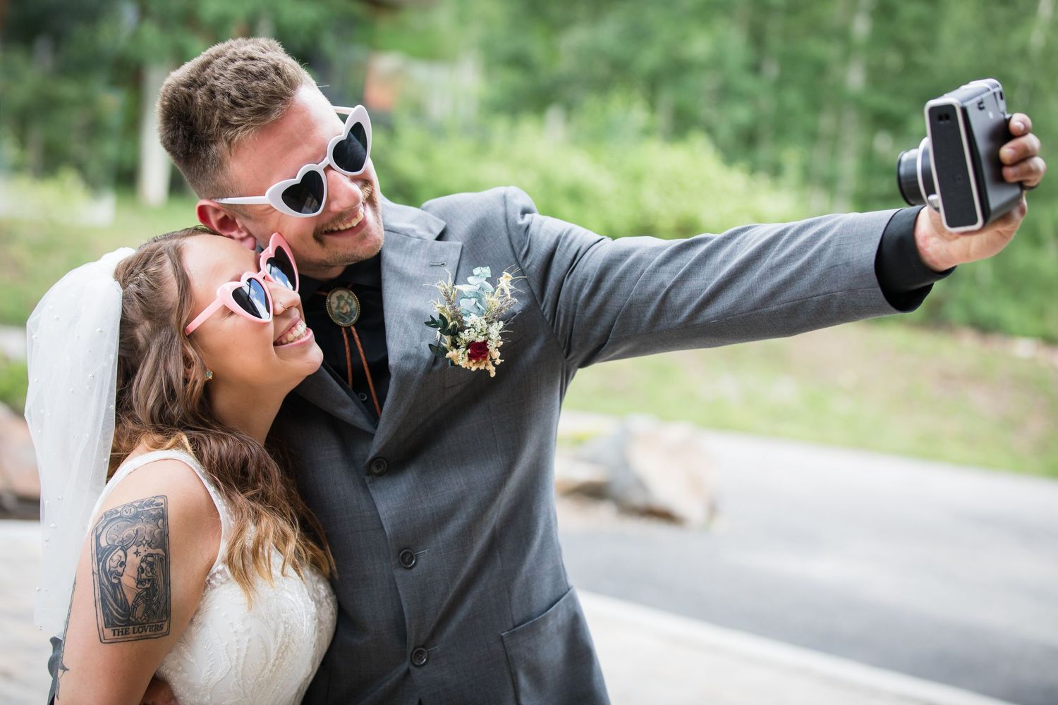 Couple wearing sunglasses takes selfie during outdoor wedding celebration.