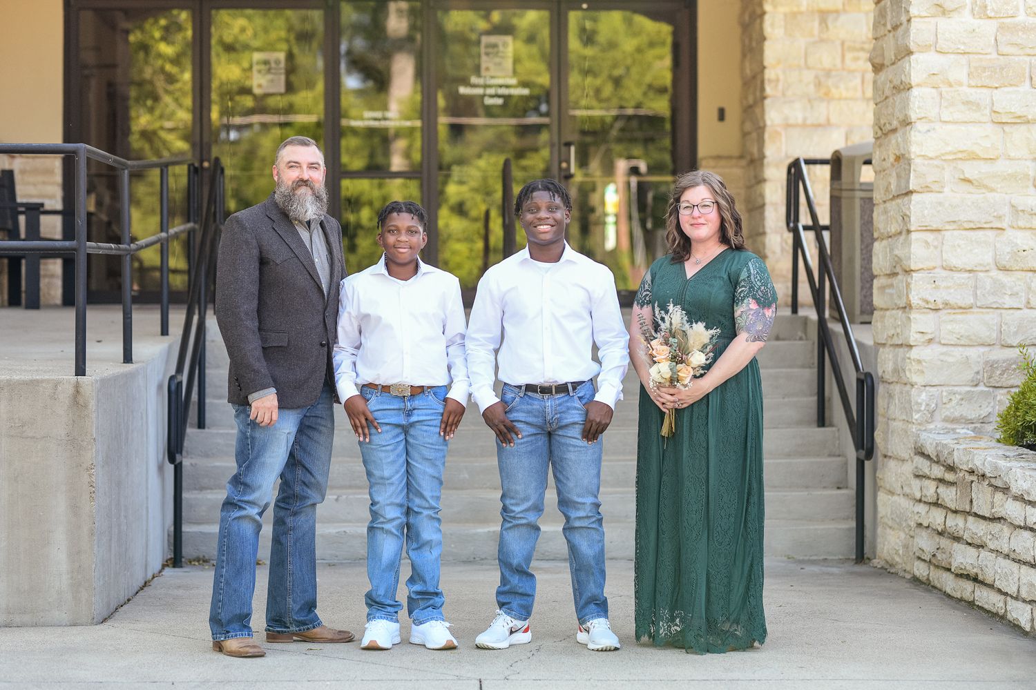 Family photo outside stone building with railings and glass doors.