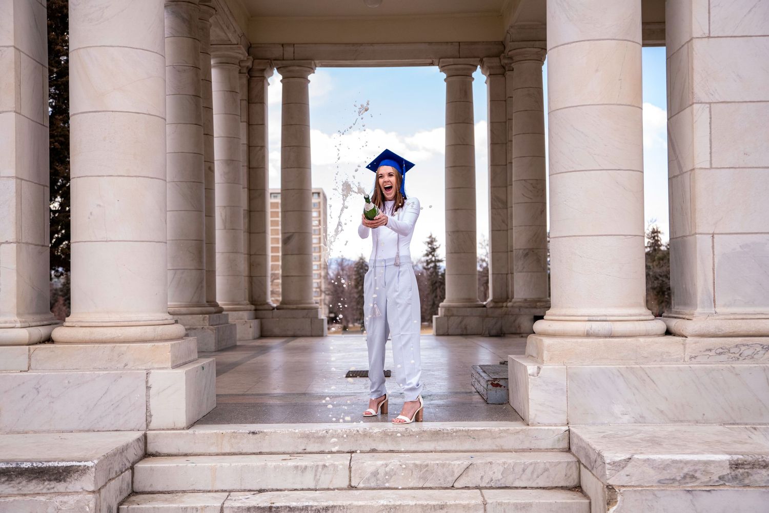 Graduate posing between classical stone columns in cap and gown on graduation day.