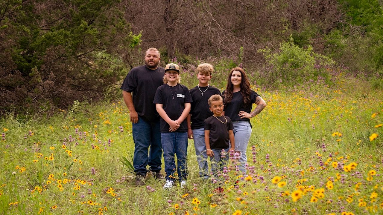 Family group photo in field of yellow wildflowers surrounded by trees.