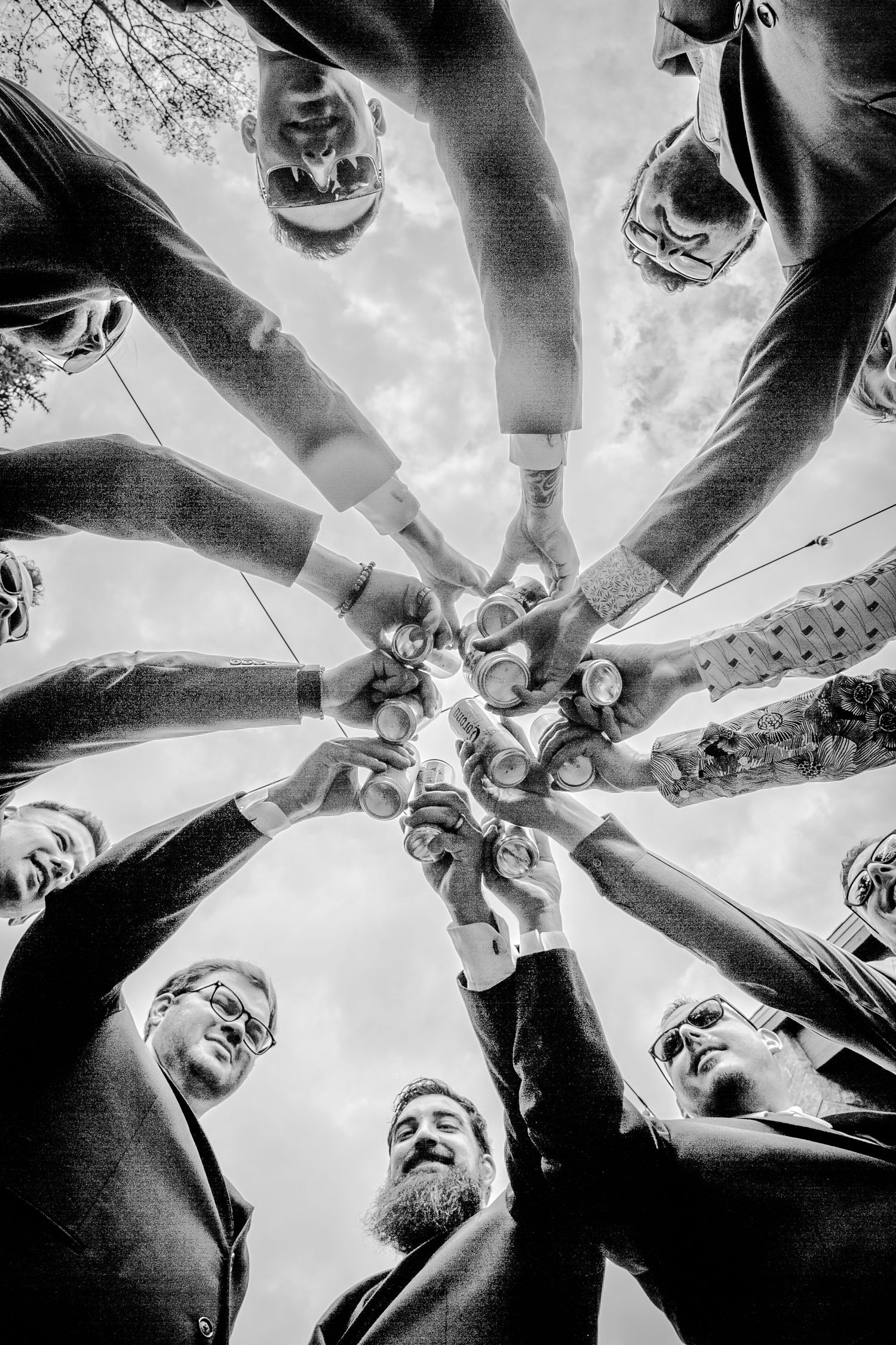 A black and white low angle shot of a group raising beer bottles in a celebratory circle formation.