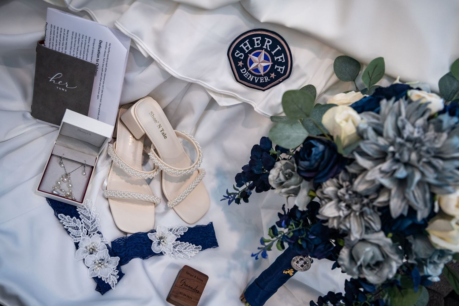 Wedding details including blue flowers, rings, and a compass on white fabric.