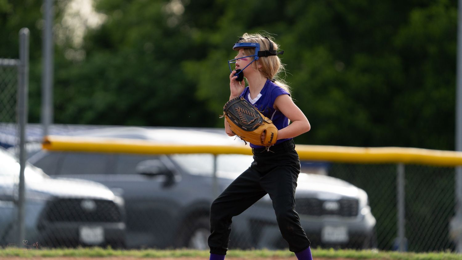 Youth softball player in purple jersey makes an intense throw during a game on an outdoor field.