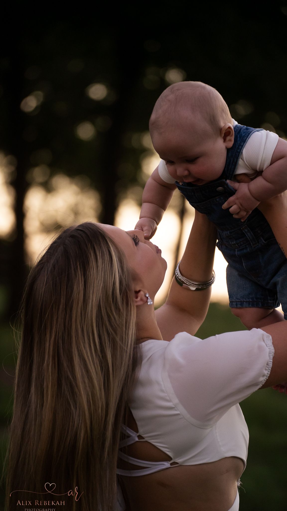 A tender moment between parent and baby captured in backlit sunset glow.