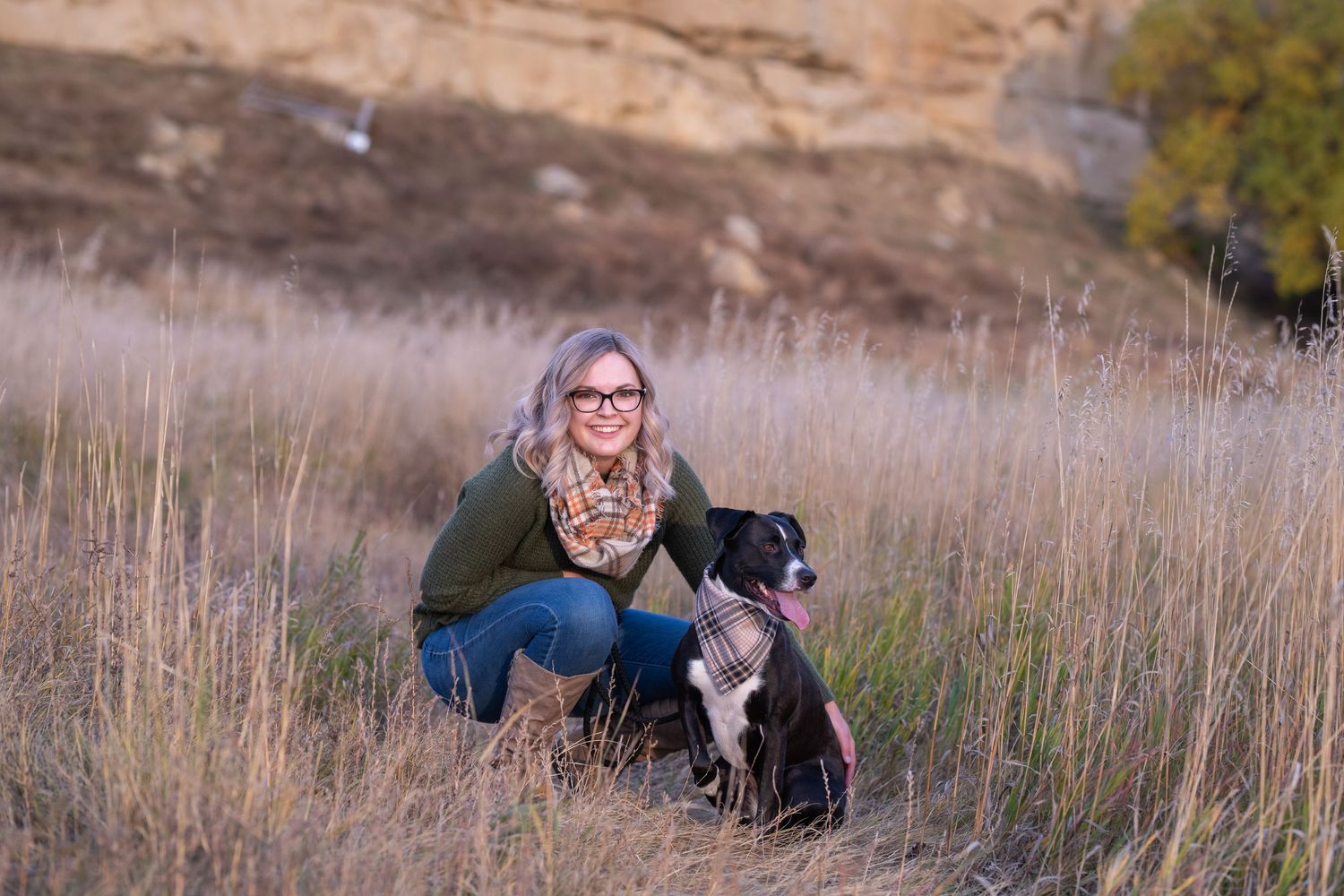 Person in glasses crouching with black and white border collie dog in tall grass.