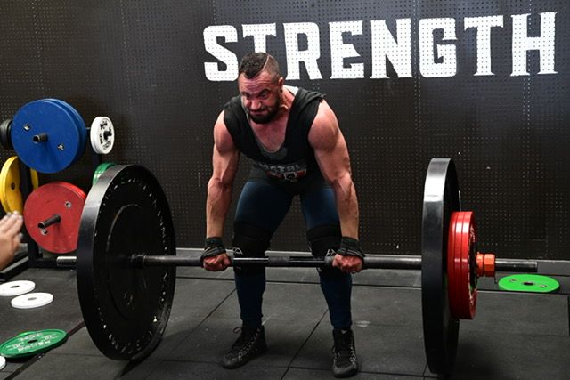 Weightlifter performing deadlift under strength sign in gym.