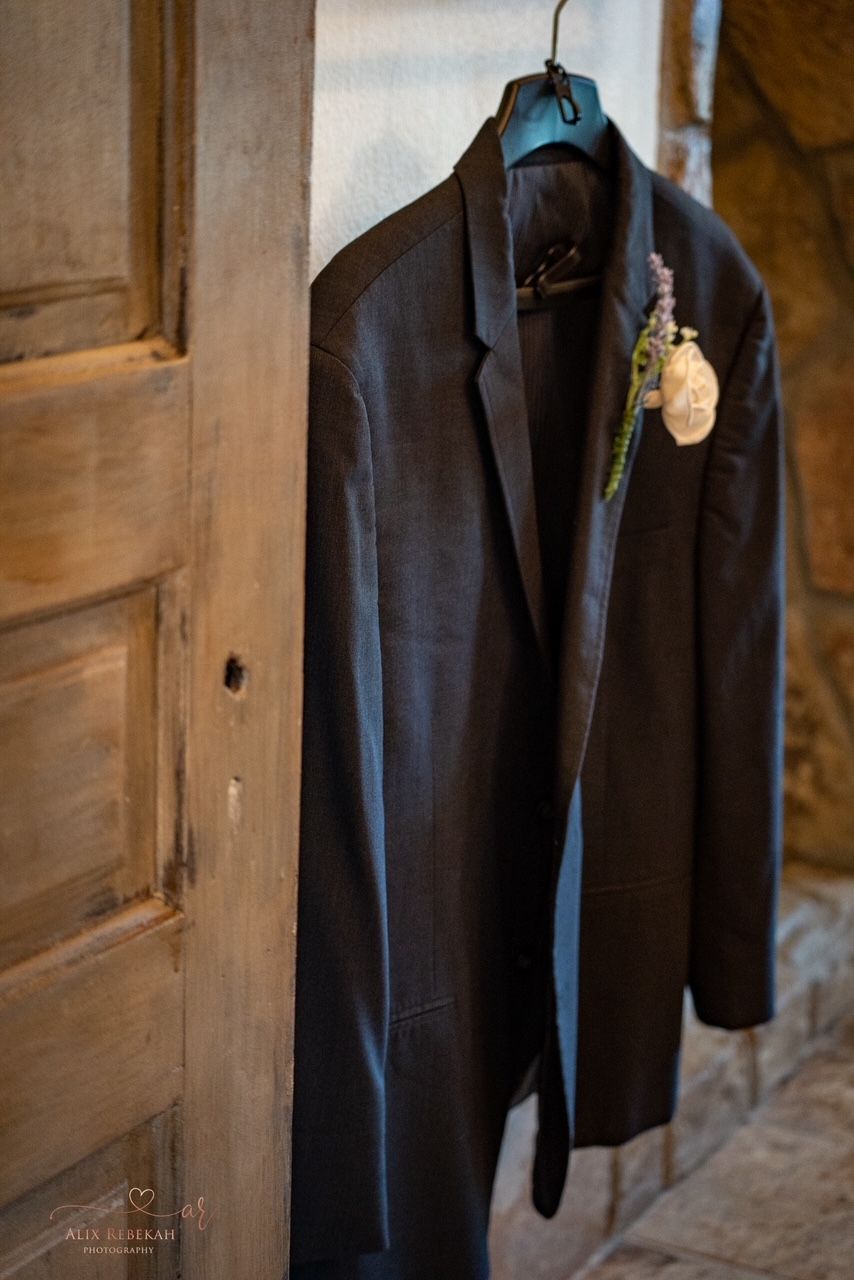 A dark suit jacket hanging on wooden door in warm, natural light.