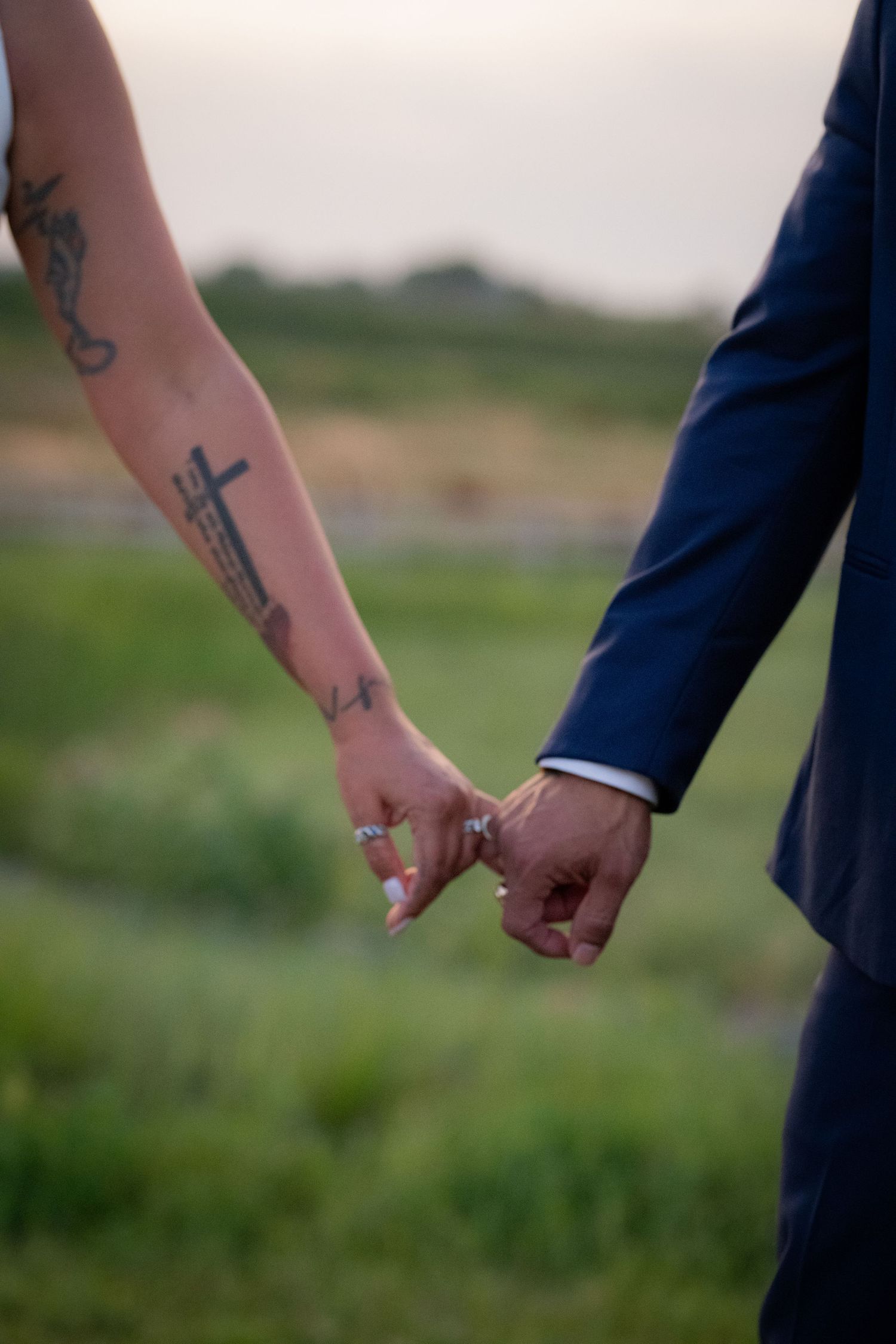 Close-up of newlyweds holding hands with one arm showing artistic tattoos against a natural backdrop.