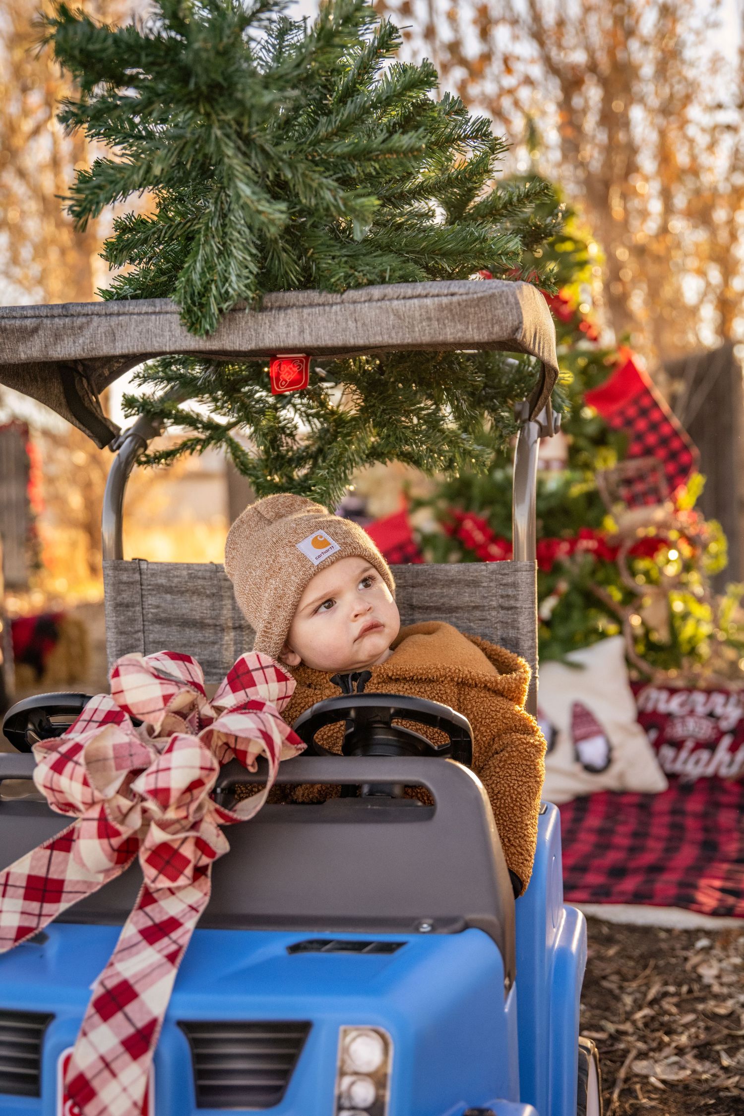 A blue toy ride-on car decorated with evergreen branches and a plaid bow for Christmas.