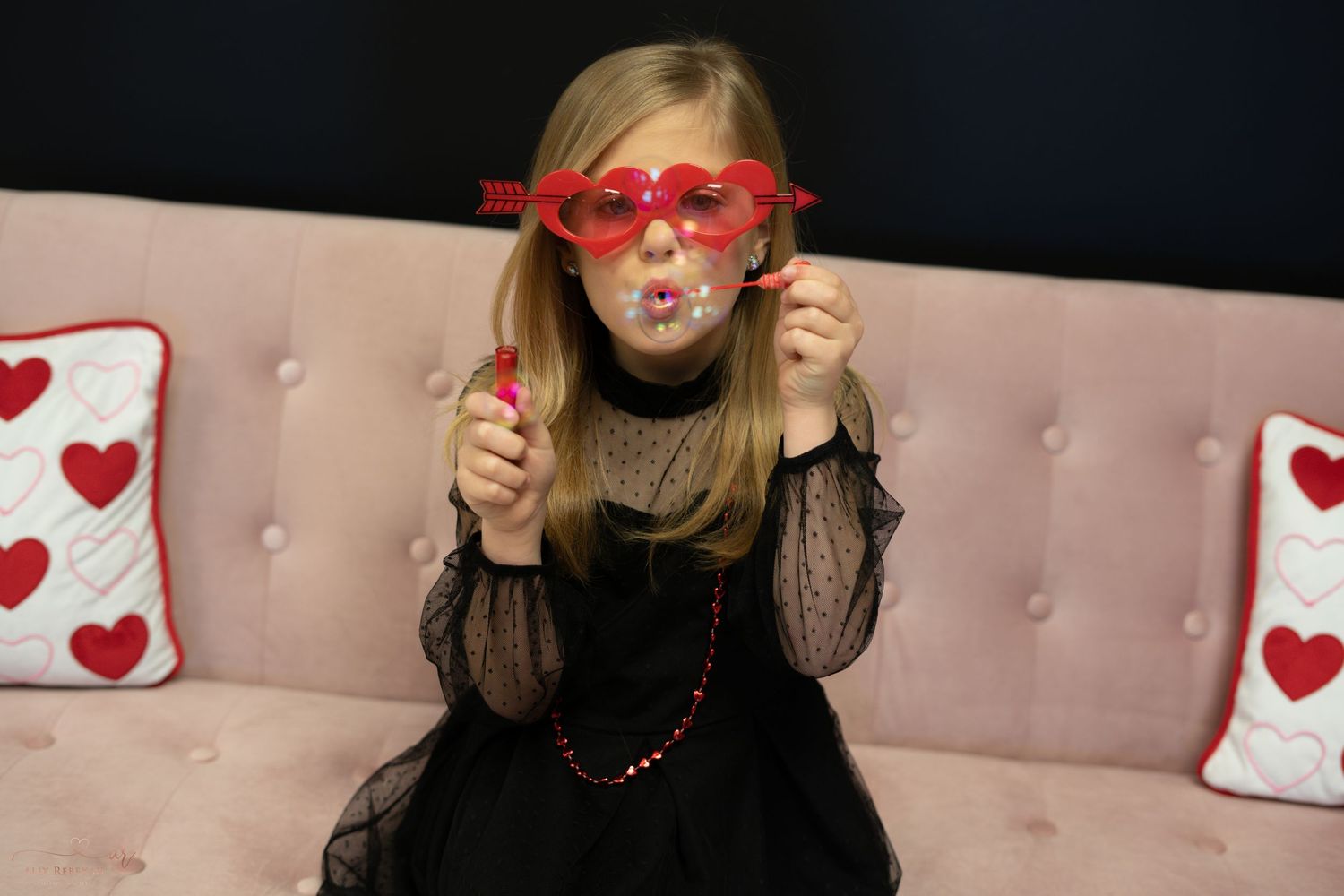 Valentine's Day photo on pink sofa with heart pillows and red heart glasses.