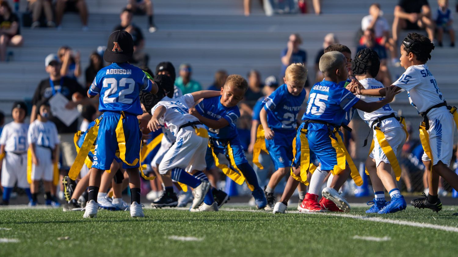 Athletes in blue and yellow uniforms compete against each other during an outdoor sports match on a sunny day.