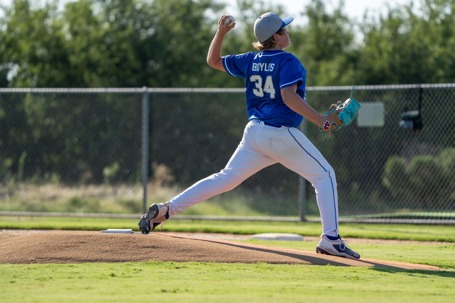 Baseball pitcher in blue uniform delivers a powerful side-arm throw on sunny outdoor field.