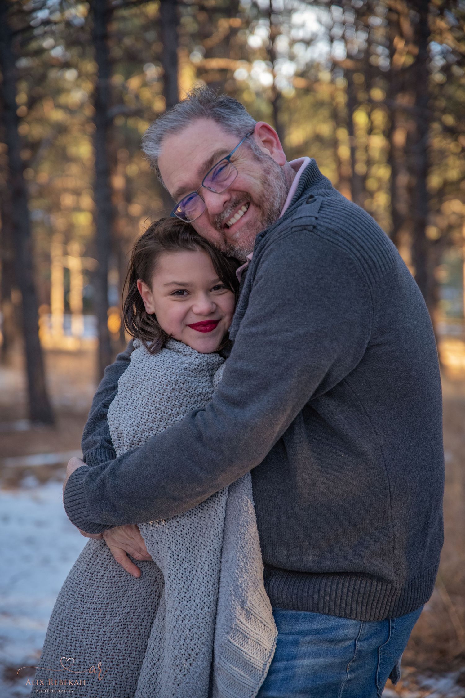 Warm embrace captured between two people wearing gray sweaters in snowy forest setting.
