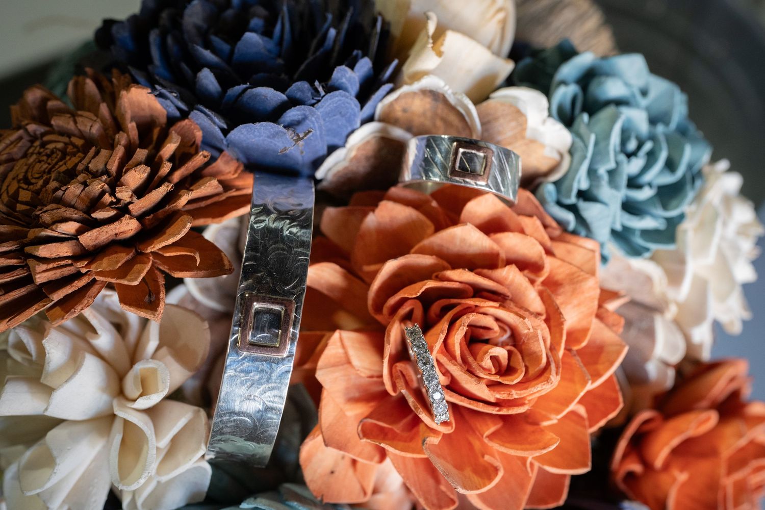 Wedding rings nestled among colorful fabric flowers in coral, blue, and cream.