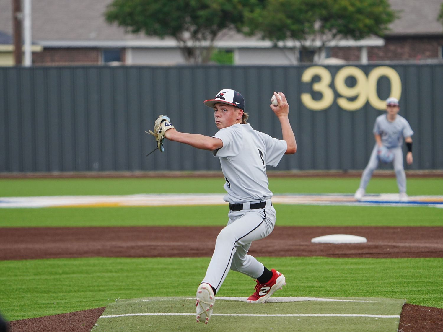 Baseball pitcher in white uniform mid-throw on a professional field with 390 ft marker visible in background.
