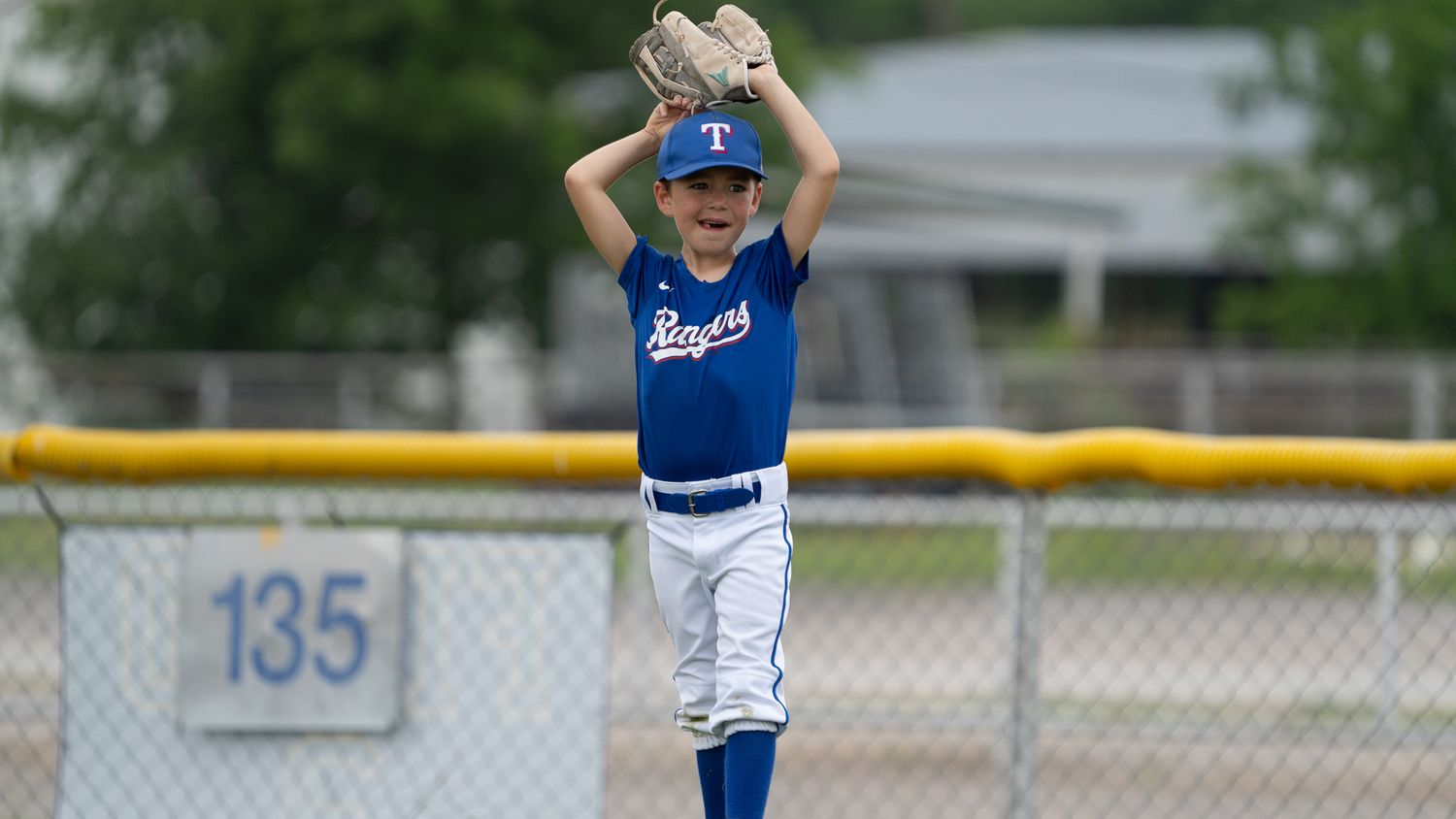 Young baseball player in blue Dodgers uniform stands ready to pitch during a youth league game on a cloudy day.