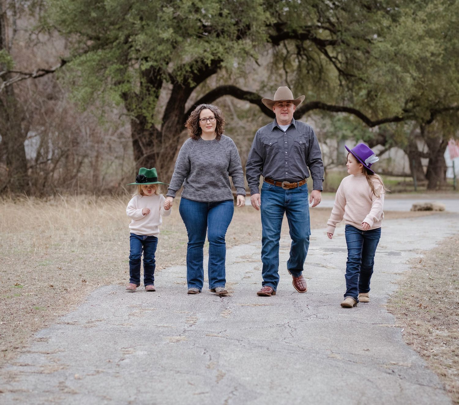 Family walking together on a gravel path under oak trees on an overcast day outdoors.