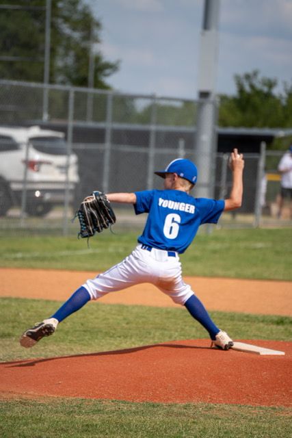 Youth baseball pitcher in blue uniform following through on delivery from the mound.
