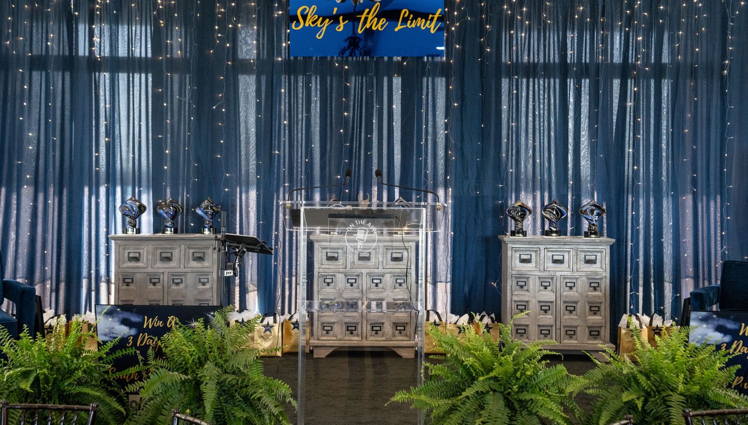 Wedding reception decor with blue draping, metallic elements and tropical greenery.