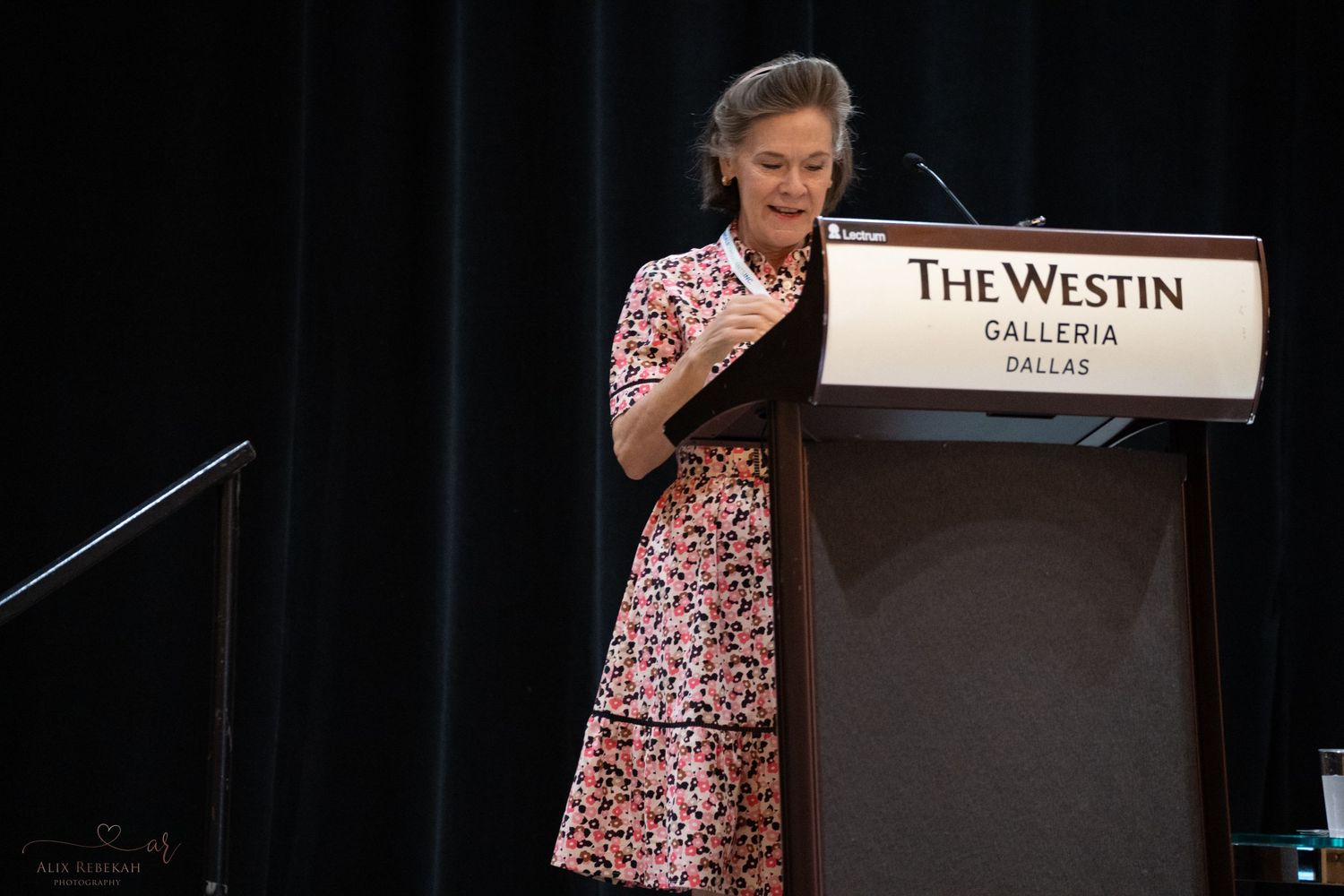 Presenter delivering remarks at The Westin Galleria podium during conference.