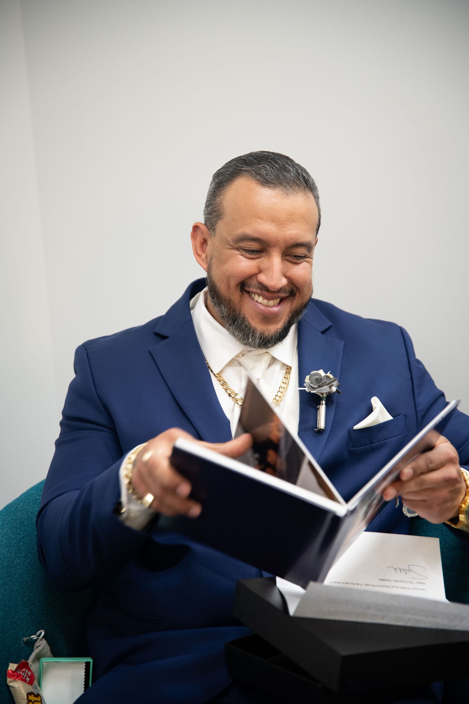 Person in navy suit reading a book while seated in teal chair.