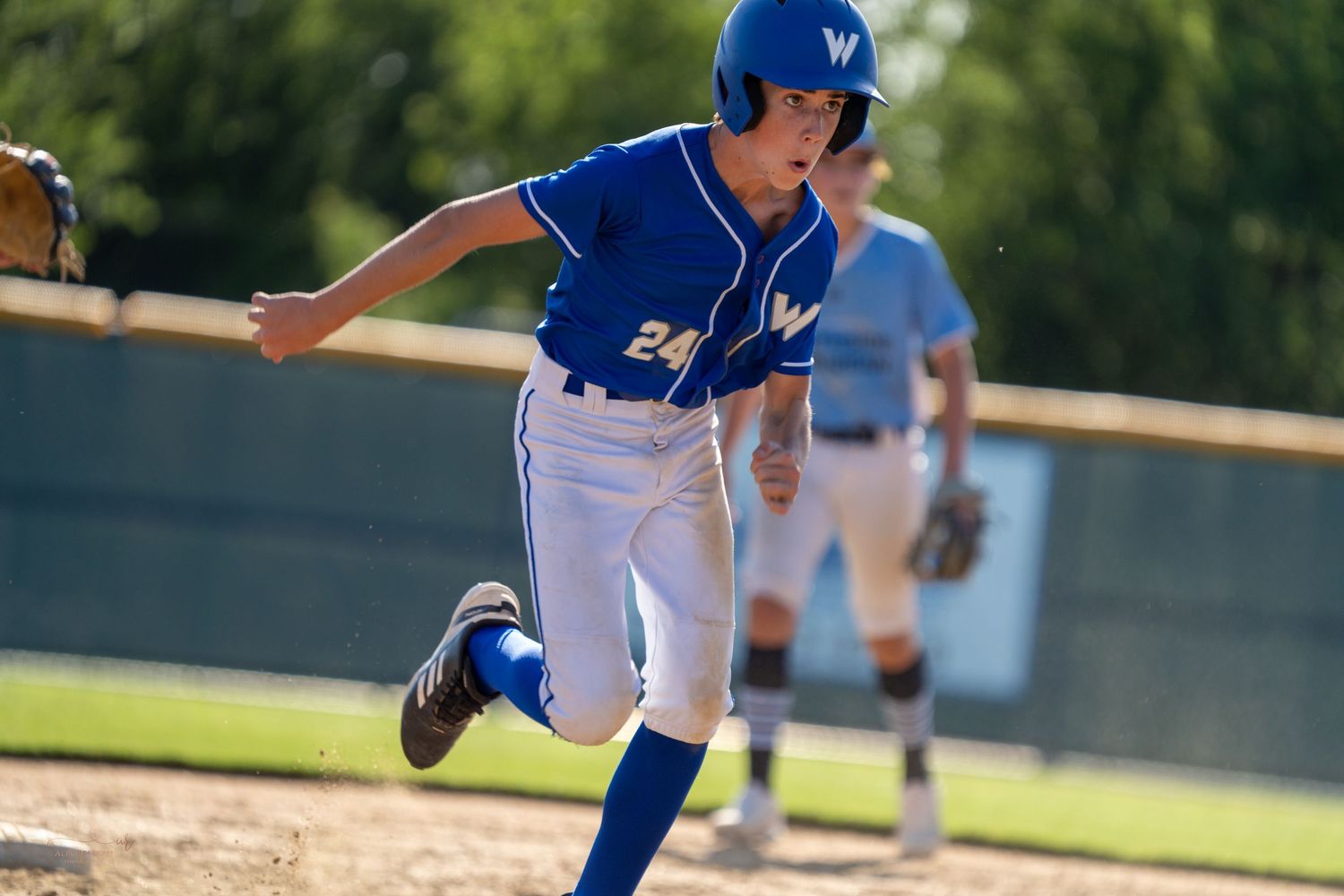 Youth baseball player in blue uniform swings bat during game on sunny day.
