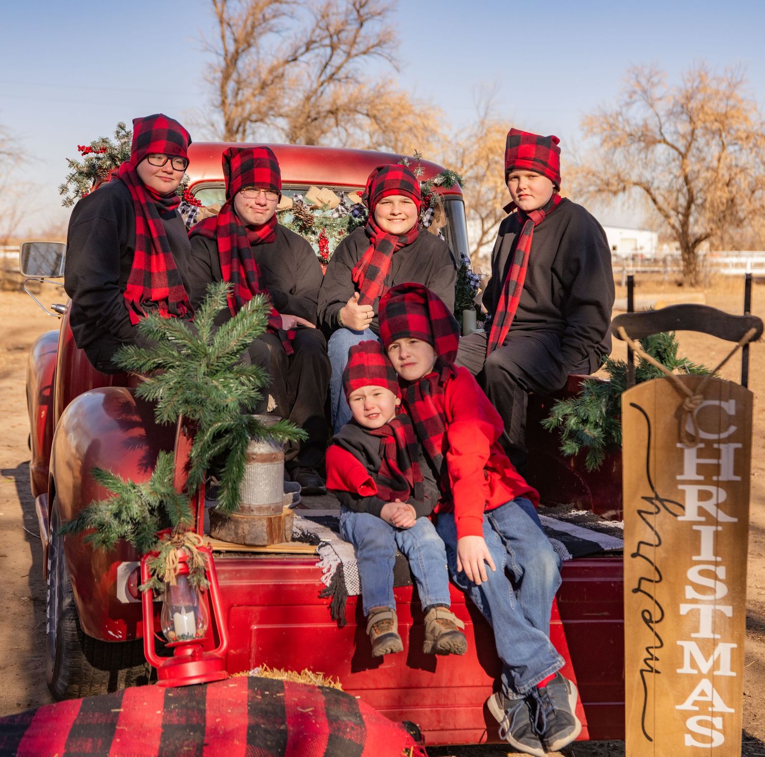 A red truck bed used for holiday photos, decorated with festive greenery and coordinated winter accessories.