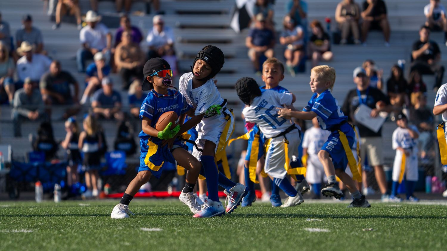 Sports teams line up across the field during a competitive match with spectators watching in the background.