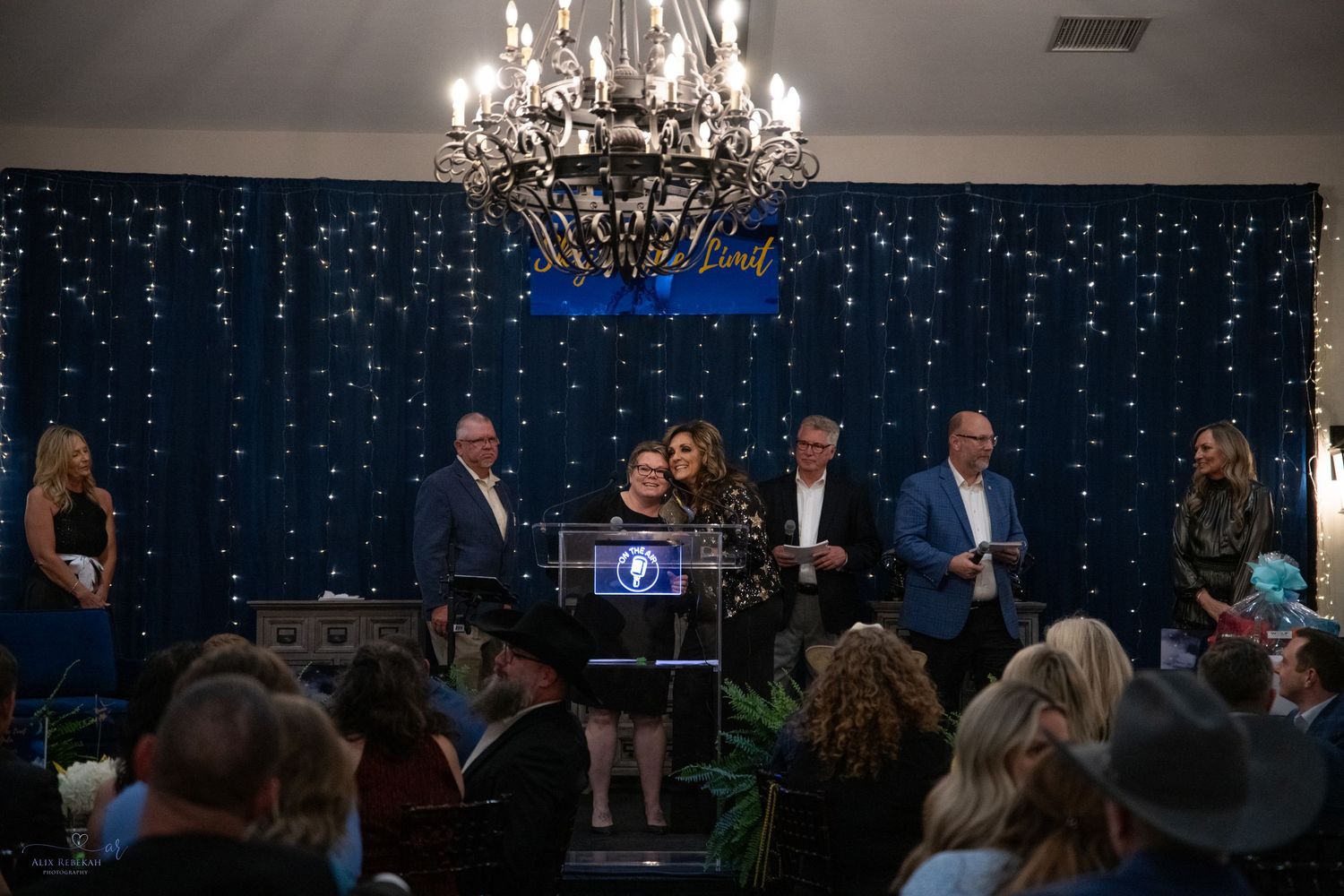 Elegant ballroom event with chandelier and blue twinkle light backdrop during evening ceremony.