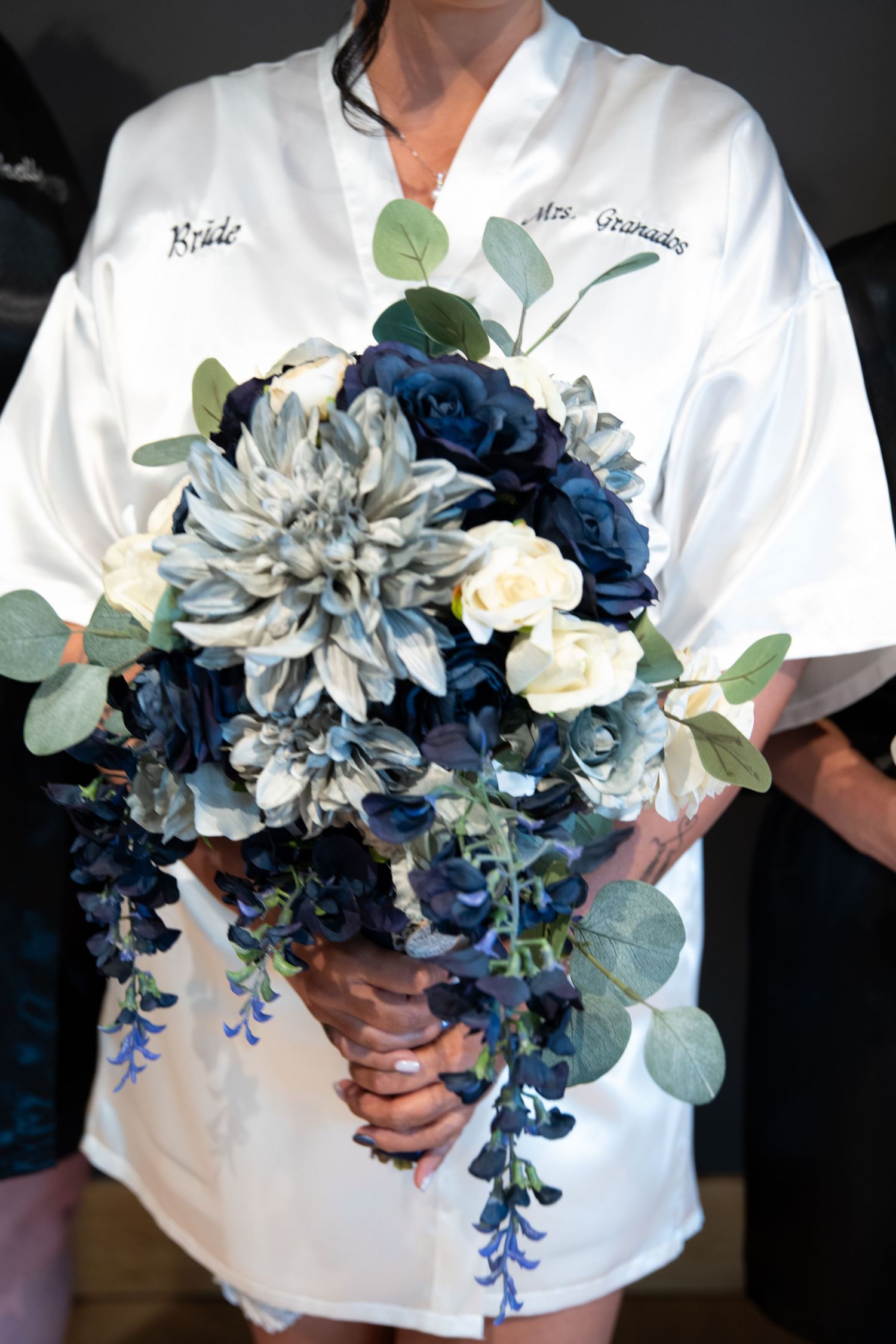 Elegant bridal bouquet with blue and white flowers and eucalyptus held against white robe.