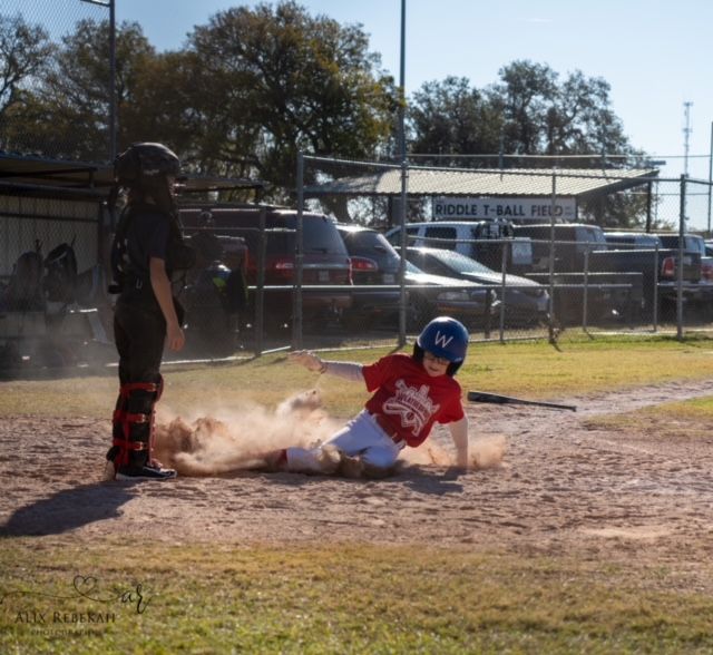 Baseball player sliding into base while umpire watches during game.